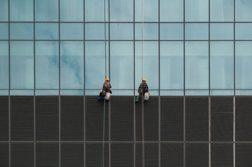 Two window cleaners suspended on ropes cleaning a modern skyscraper facade.